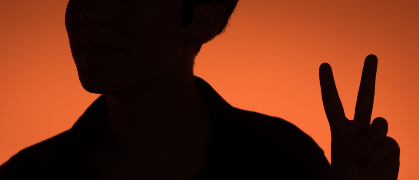 Silhouette of a person holding up two fingers in a peace sign, against an orange background