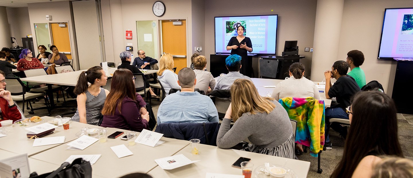 classroom full of students, watching a professor at the front of the room