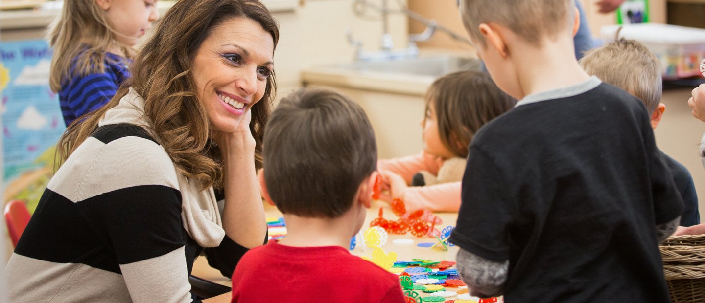 Special Education ABA Female teacher with five young students playing with colorful toys in a classroom.