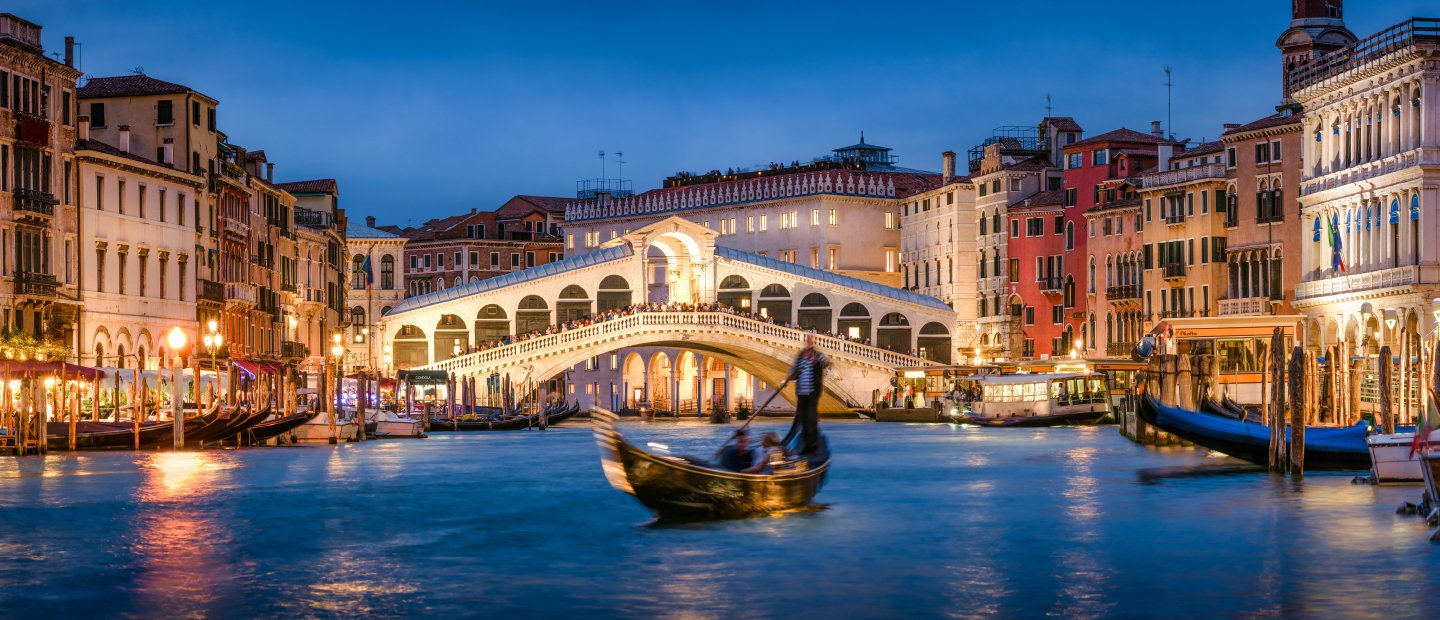 People on a gondola in a canal at night in Italy.