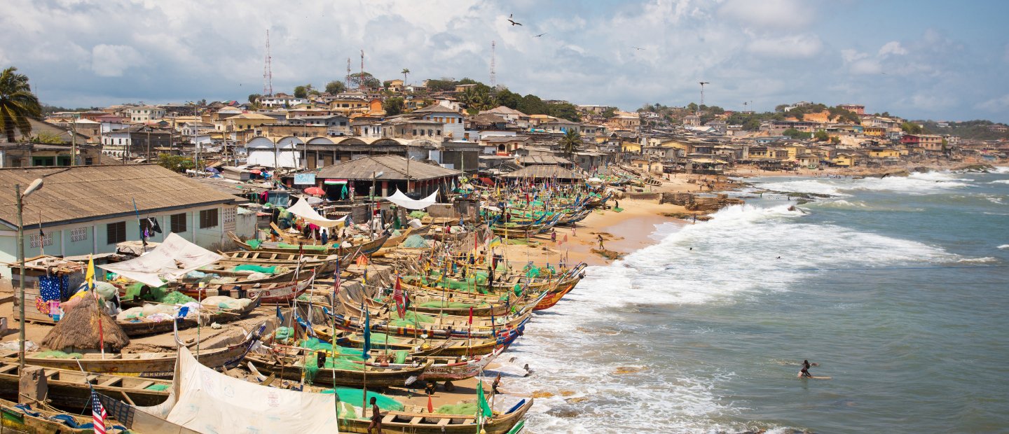 An aerial photo of a town on the water in Ghana, with boats lined up on the beach.