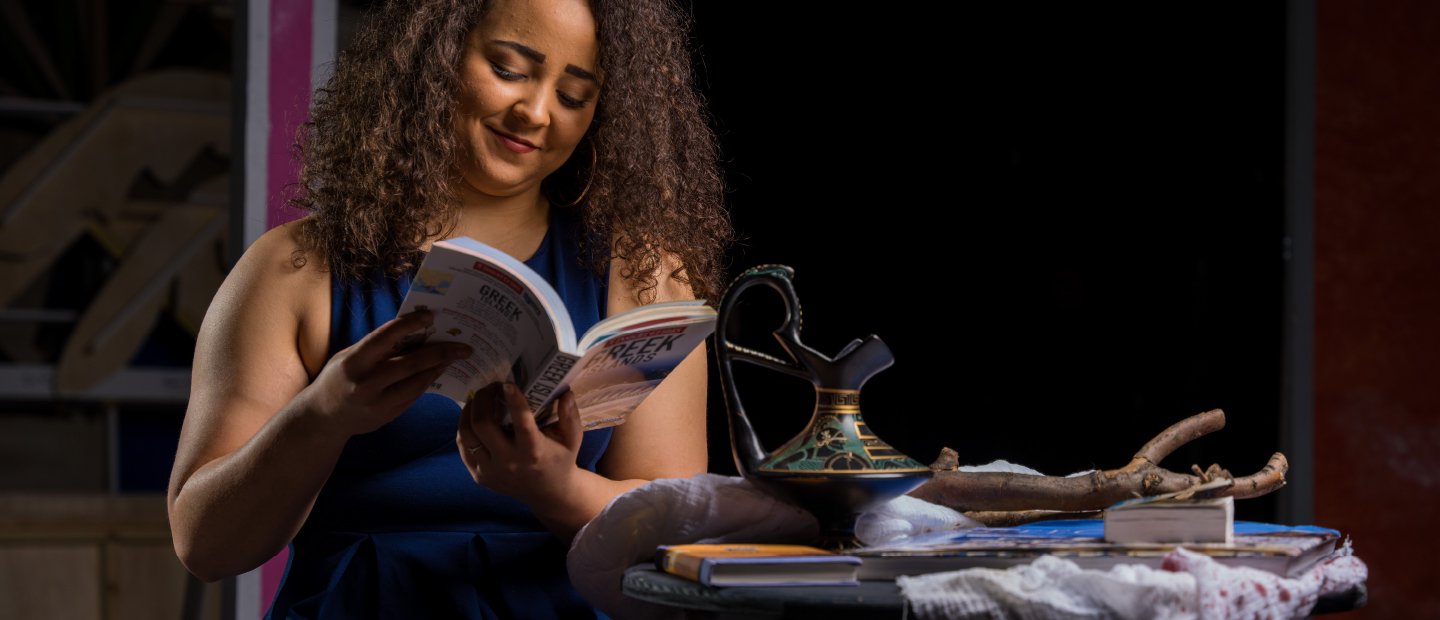 A woman reading a play near a table of stage props.