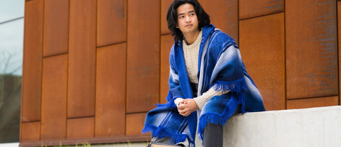 A man seated on a ledge outside of a brown building.