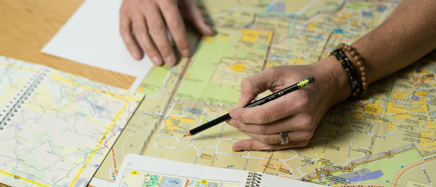 A person holding a pencil over a location on a map.