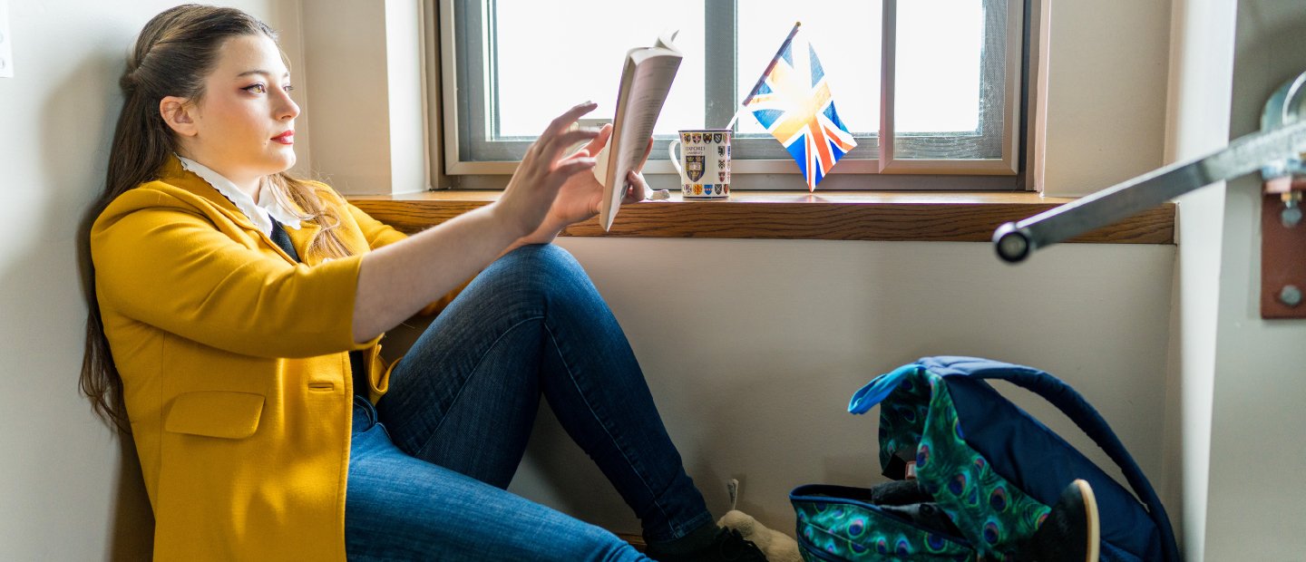 A woman sitting on the floor in a room, reading a book.