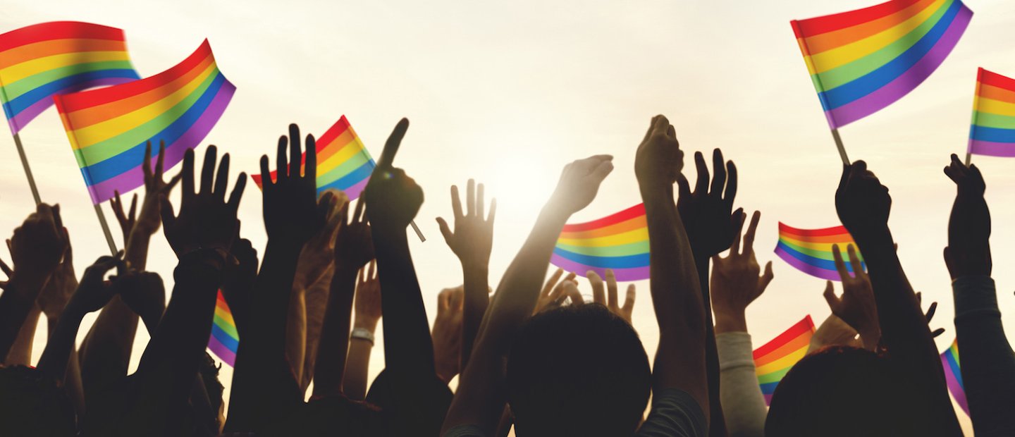 Hands pointing in the air and waving rainbow colored flags outside.