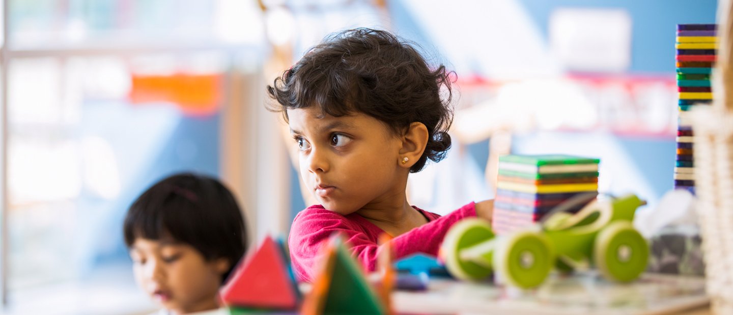 Curriculum A young girl playing with bright colored stacking blocks.