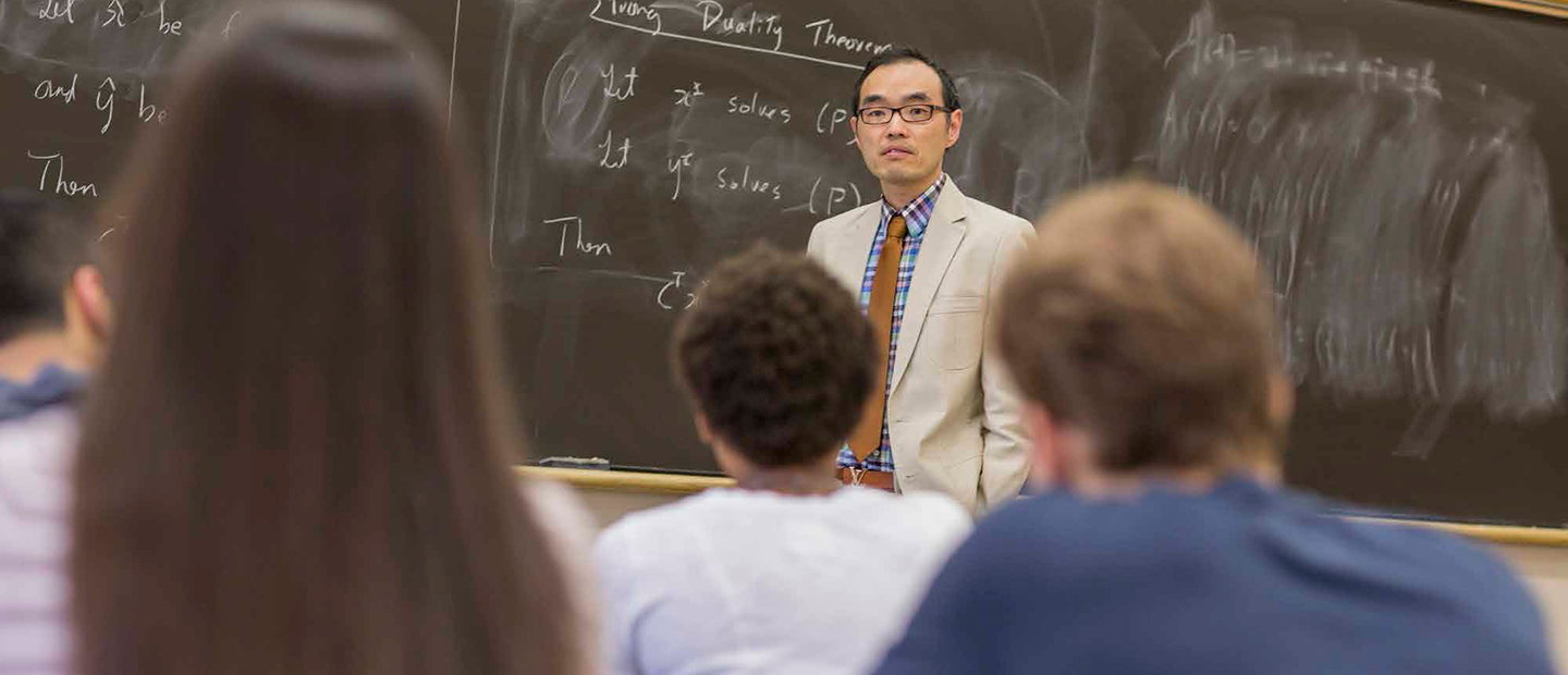A professor standing in front of a chalkboard in front of students