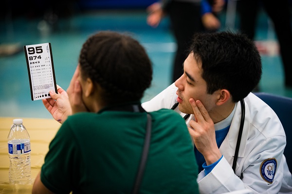 An OUWB student helps a student with an eye exam.