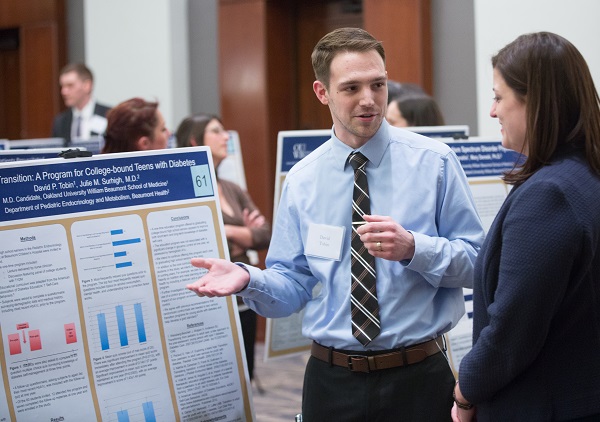 An M4 presents his research poster to a faculty member at the annual Capstone Colloquium