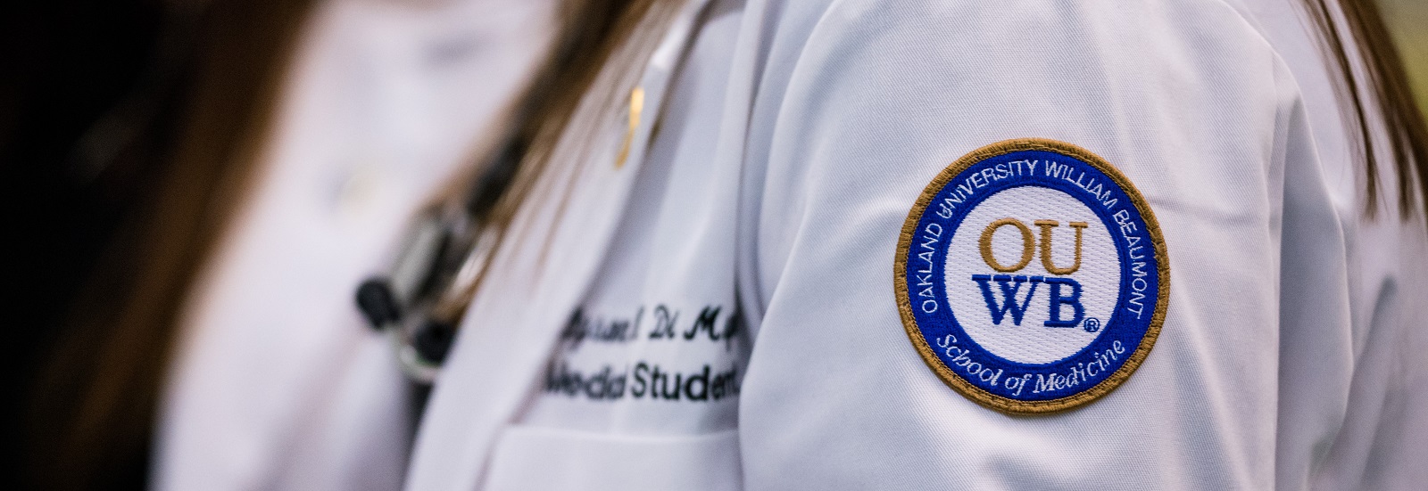 A close-up photo of a white coat with the OUWB patch in focus.