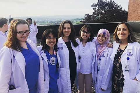 six women in white lab coats standing on a rooftop