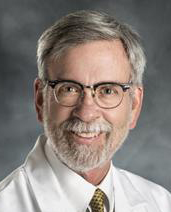 man wearing glasses and a white lab coat, smiling at the camera