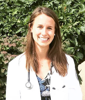 woman in a white lab coat standing outside, smiling at the camera