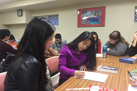 Hispanic Outreach Services mentors helping students with homework in a classroom