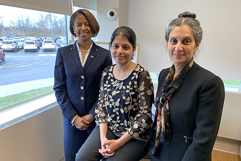 three women in professional attire posting in a room with a window