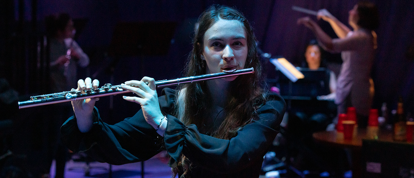 Female student playing the flute on stage, looking directly into the camera