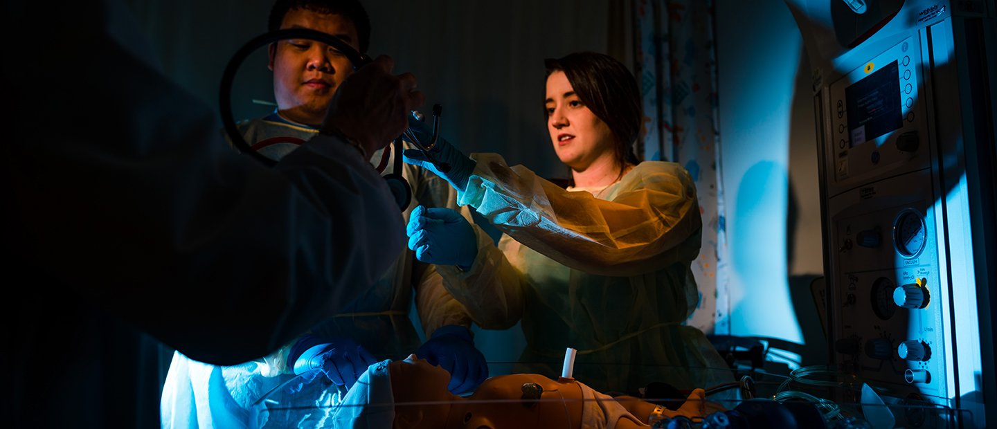 two students practicing with medical equipment in a dark room