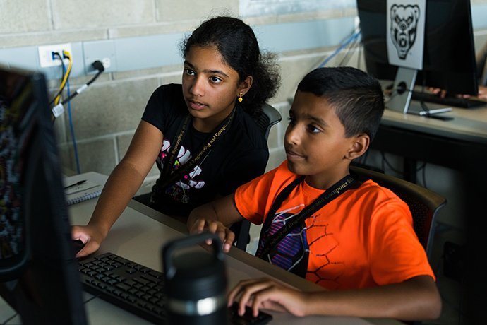A boy and a girl looking at the computer monitor