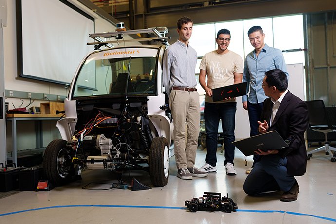 A professor and three students lookng at a robotic car