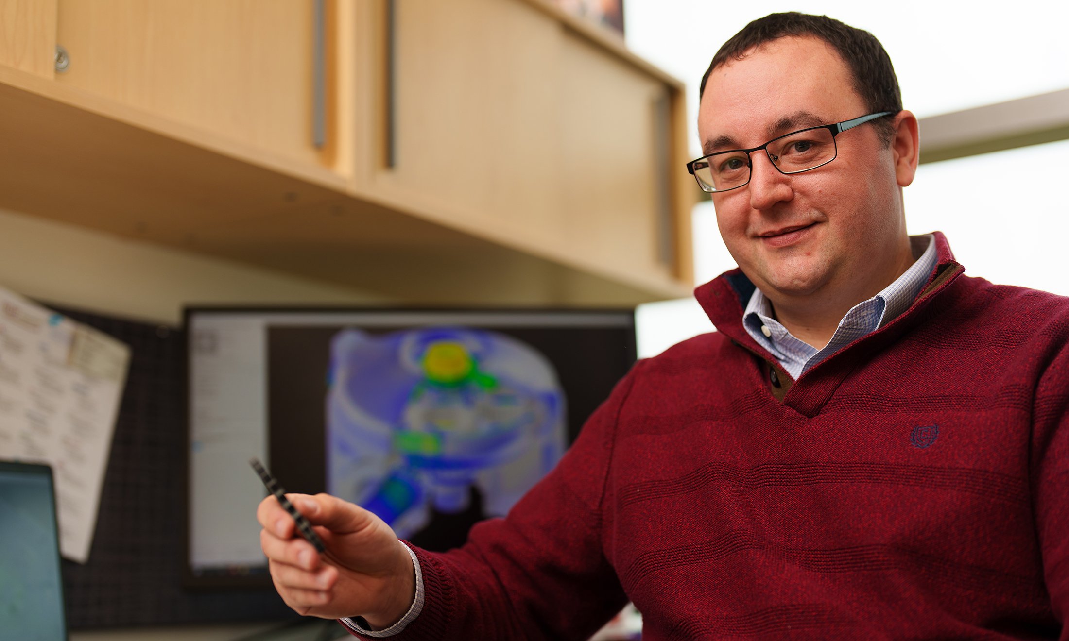 Swinging-Into-Gear-standard.jpg A man sitting at his desk holding a metal gear