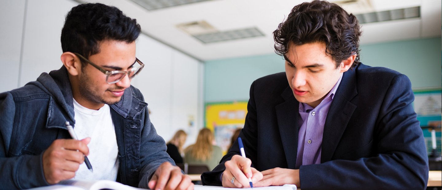 Post-Master’s Certificate in Higher Education two young men seated at a desk in a classroom, writing in notebooks