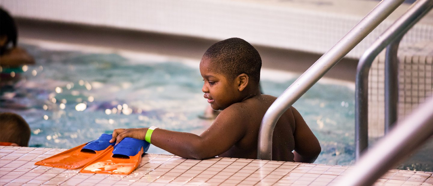 About OUCARES A young boy holding flippers, standing in a pool.