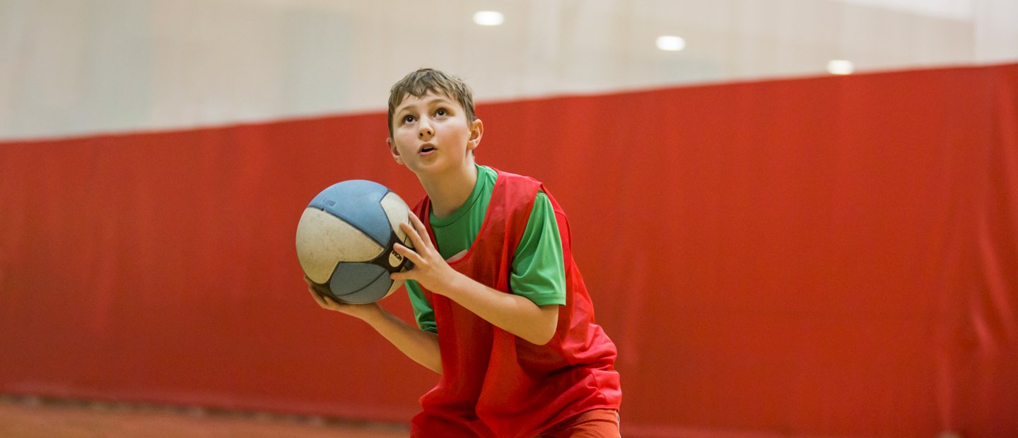 A boy in a red jersey holding a basketball on a court.