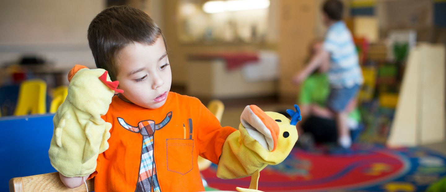 Summer Camps A young boy playing with two sock puppets in a classroom.