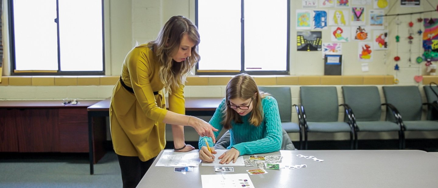 Employable Skills Training A student writing at a desk while a teacher looks over her shoulder and helps.