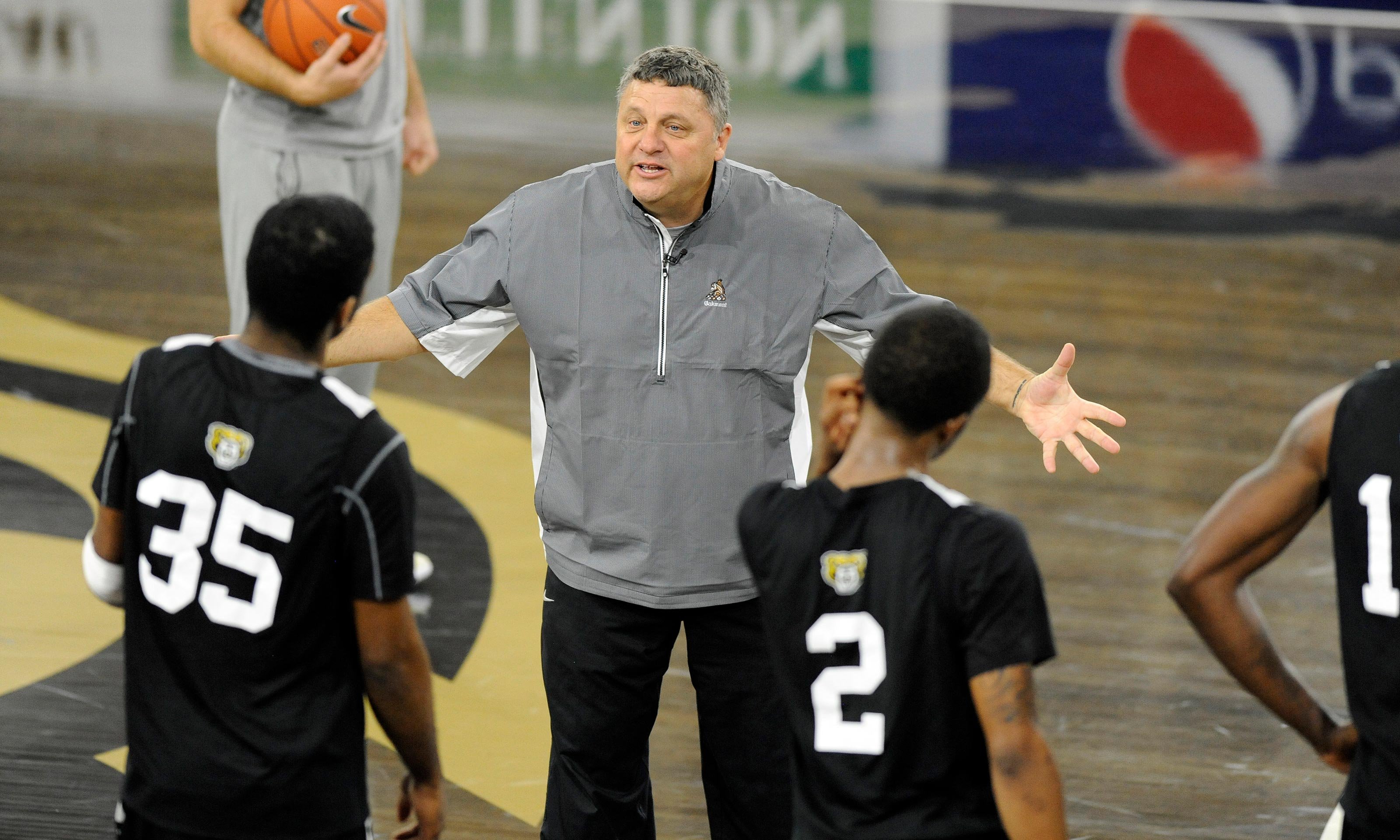 Greg Kampe coaches two players on the basketball court in the O'rena.