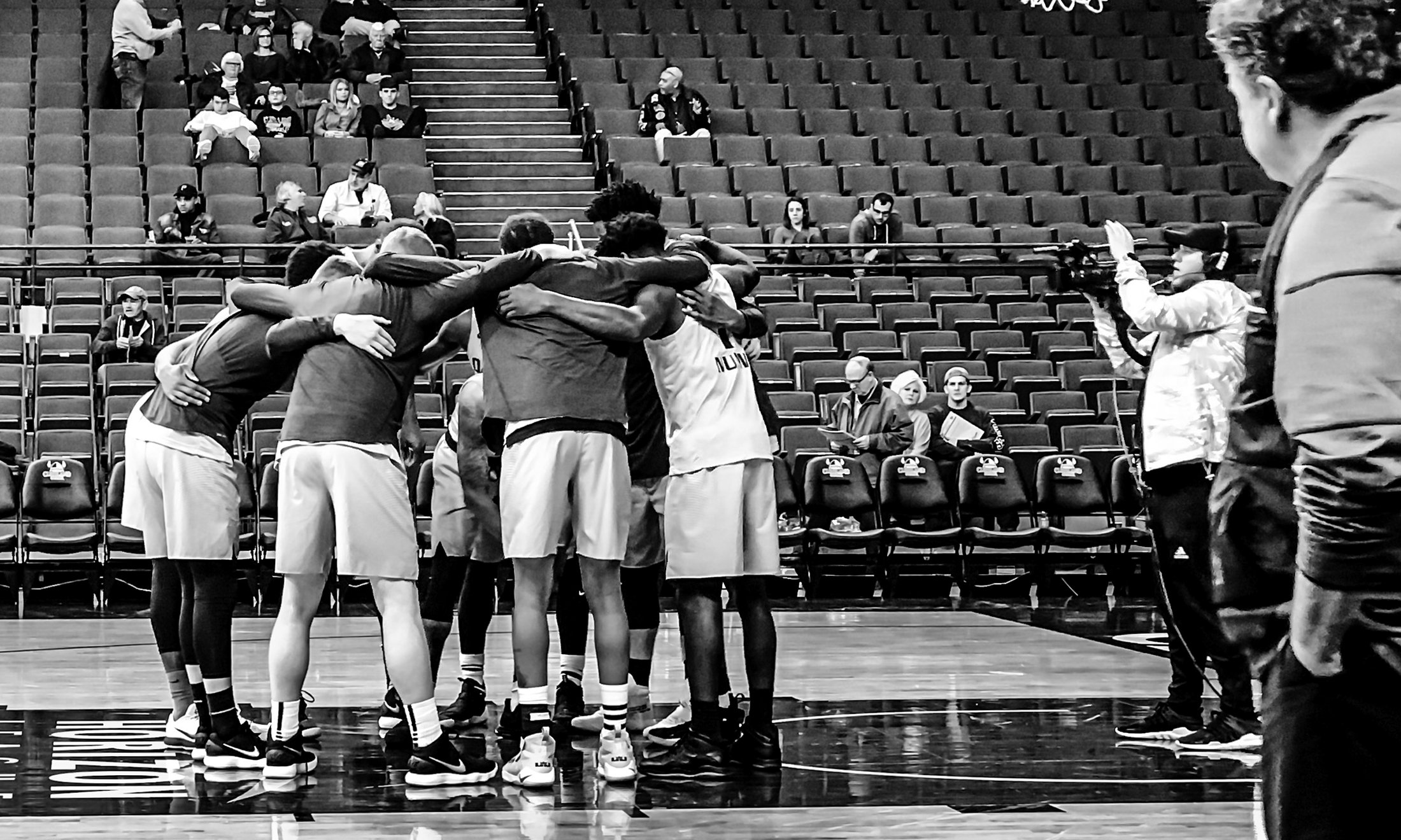 Black and white photo of men's basketball team before a game with coach kampe watching them