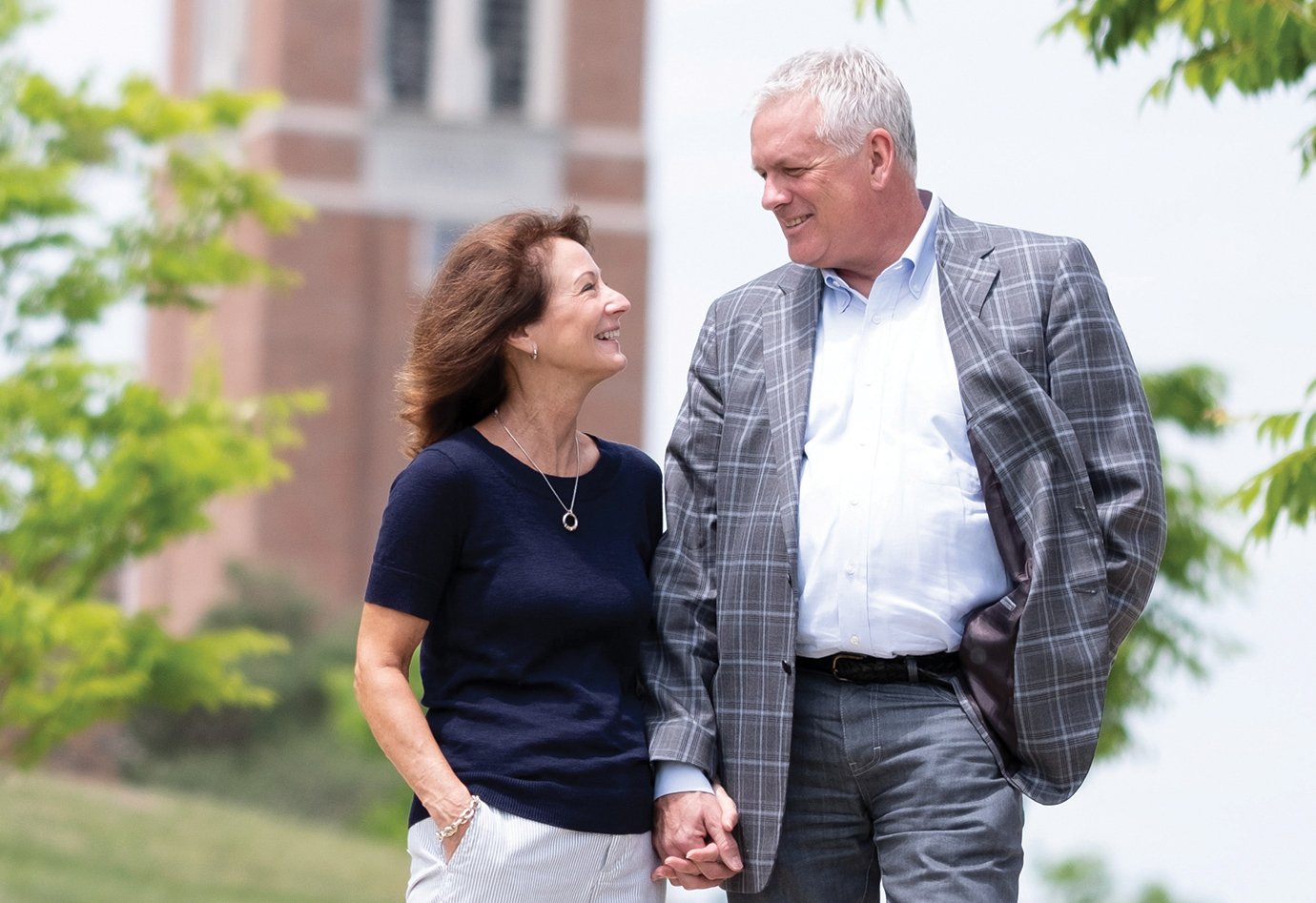 Ken and Kim Janke stand in front of Elliott Tower on campus looking at each other and smiling holding hands