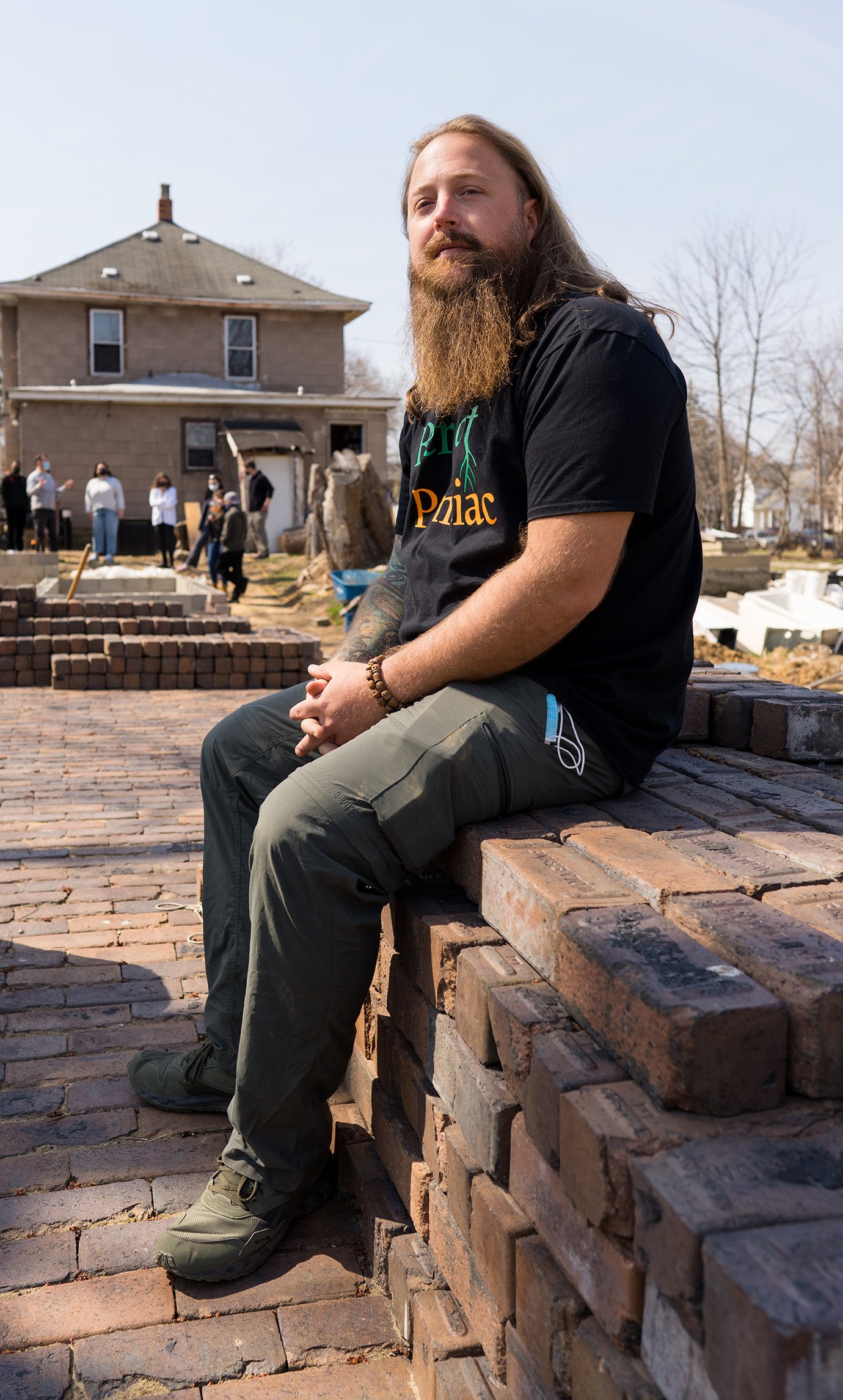 A man sitting on a ledge with a house and people in the background.