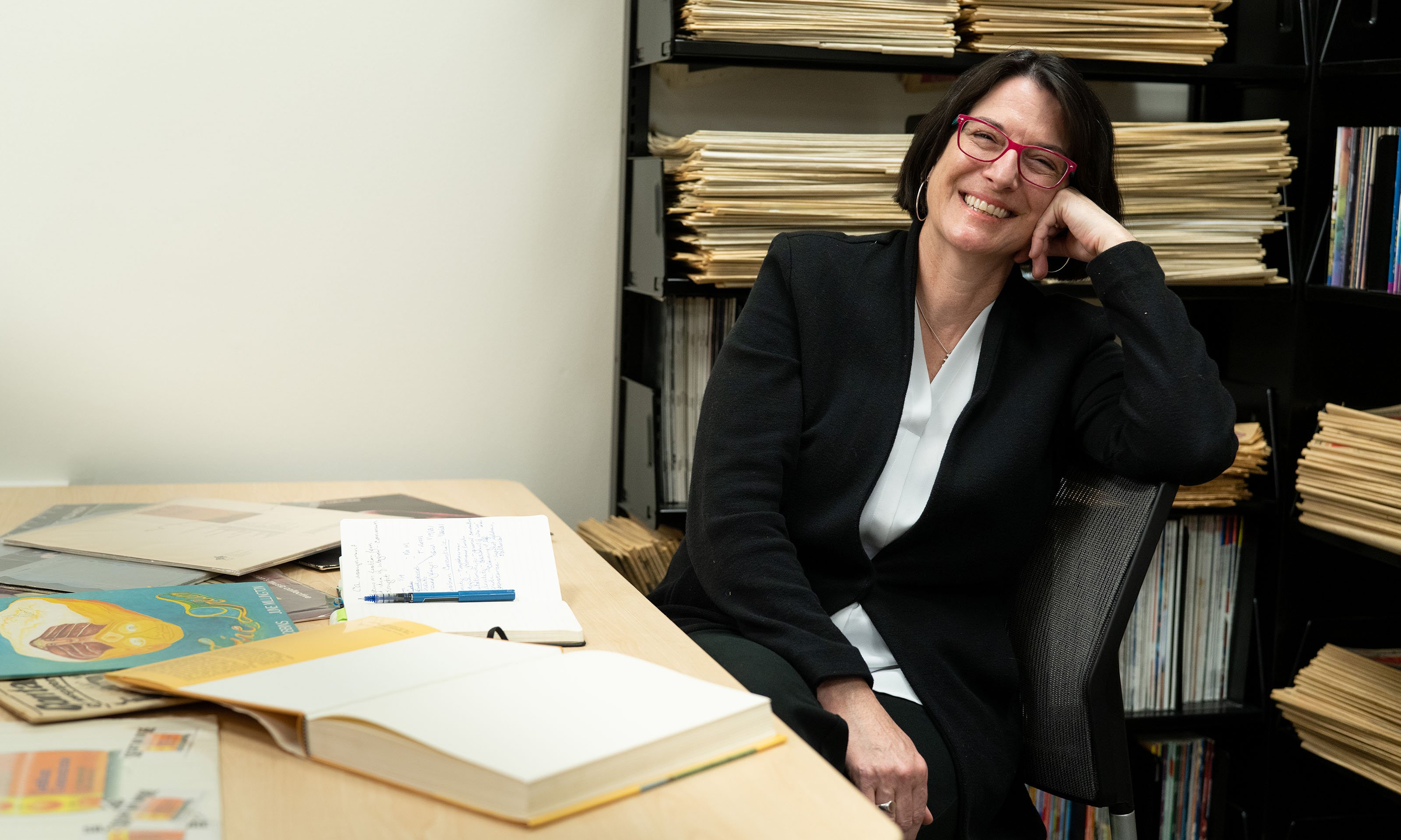 Woman sitting and smiling with record albums and books open on table