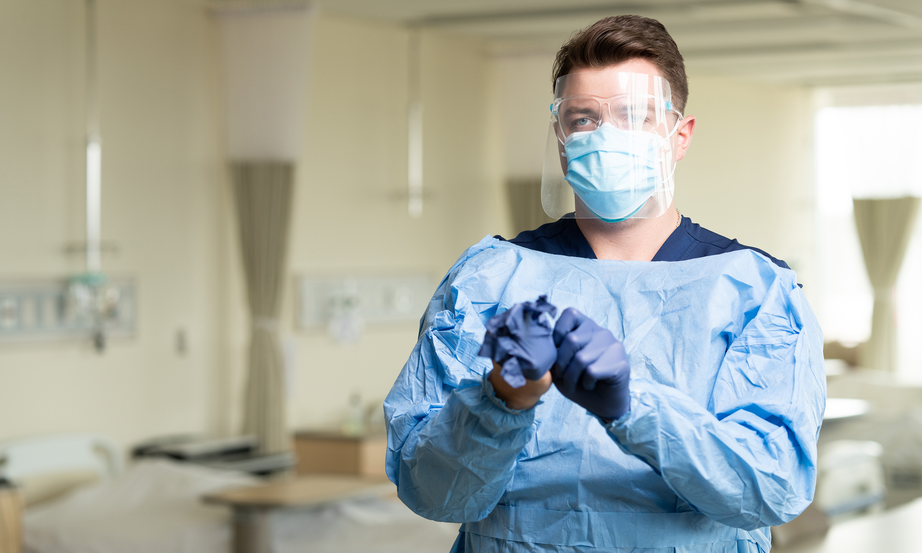A man wearing aN95, surgical mask, face shield and gown donning gloves.
