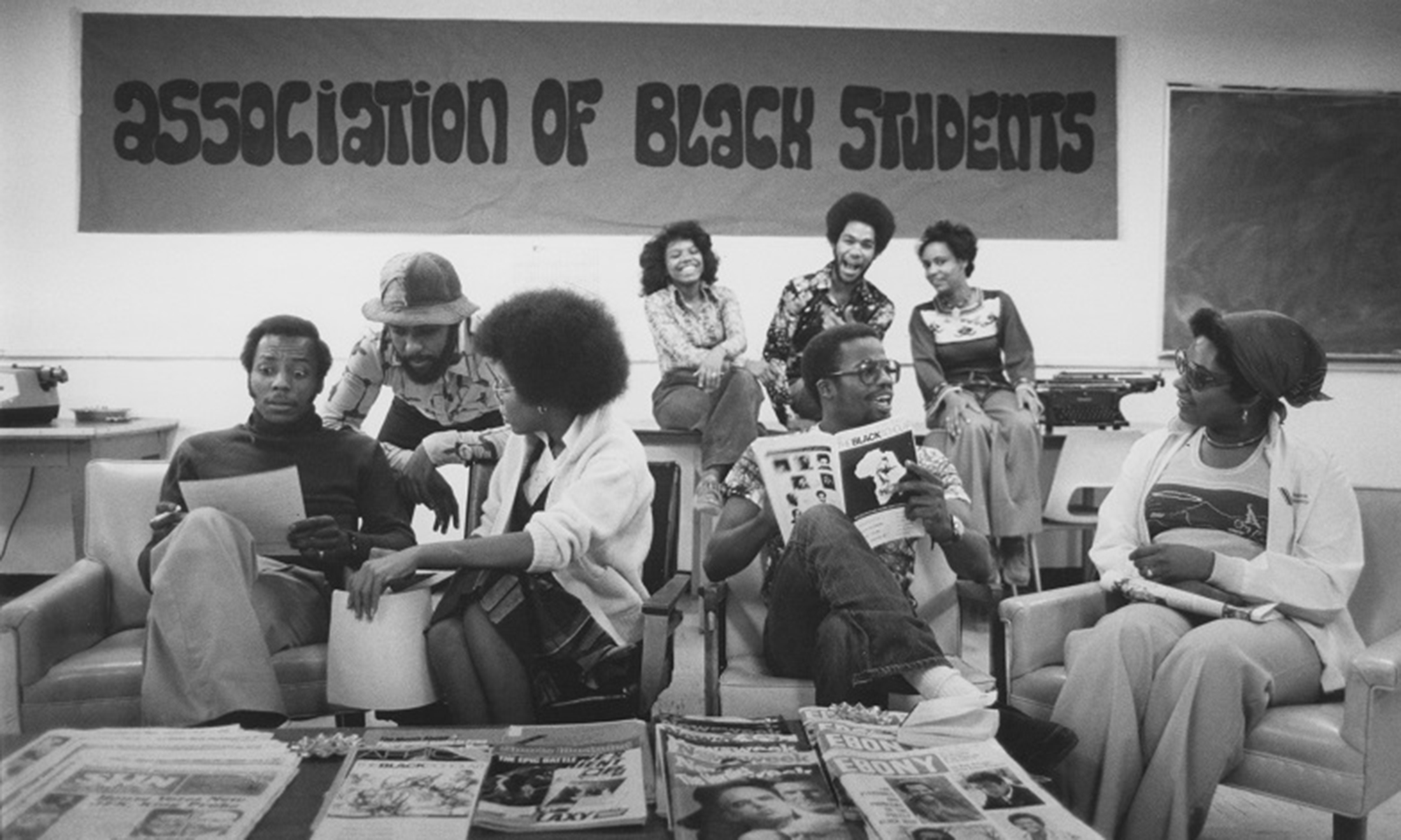 A group of students sitting around on couches, tables and chairs in front of a sign that reads, "association of black students"
