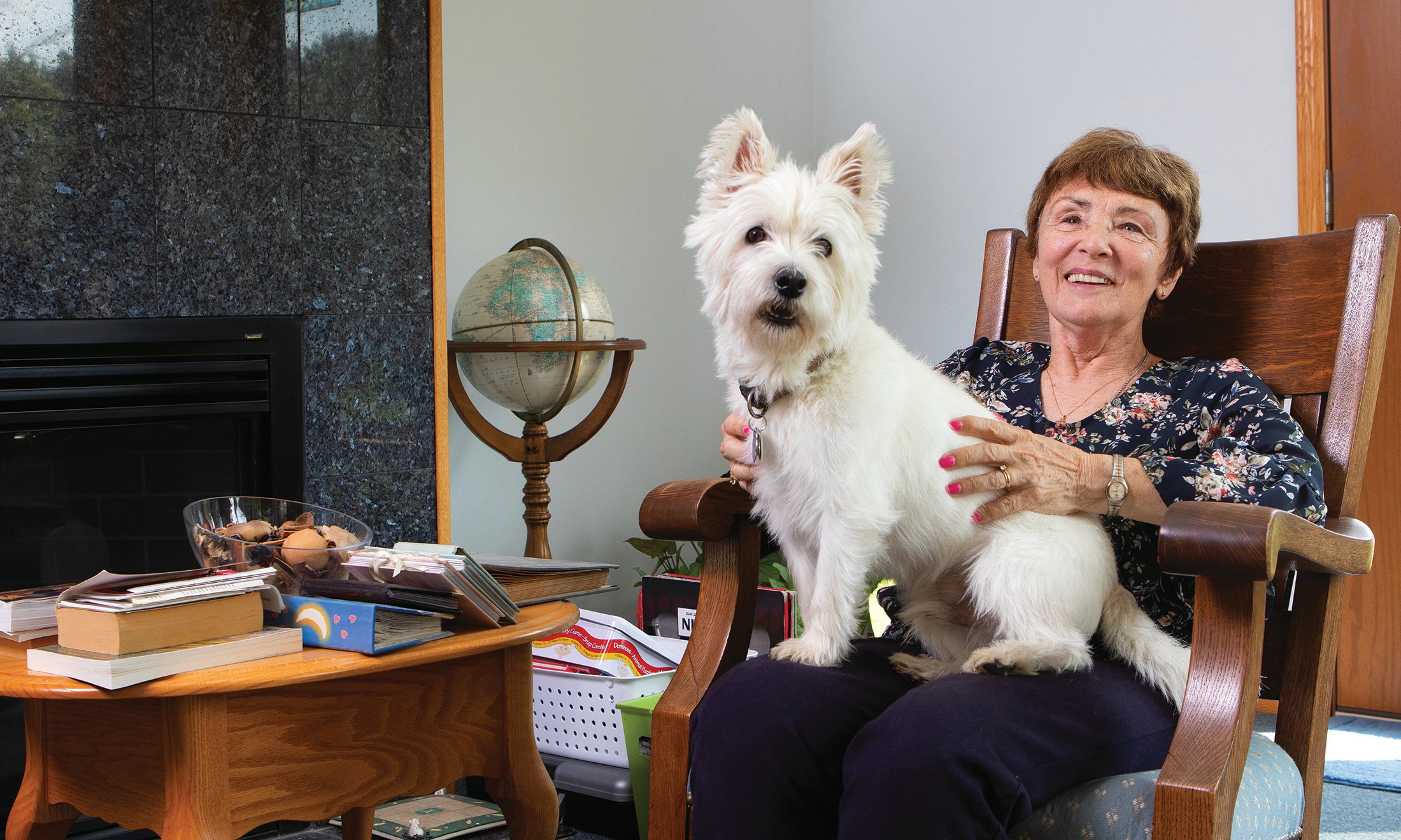 A woman in a chair with a white dog sitting on her lap.