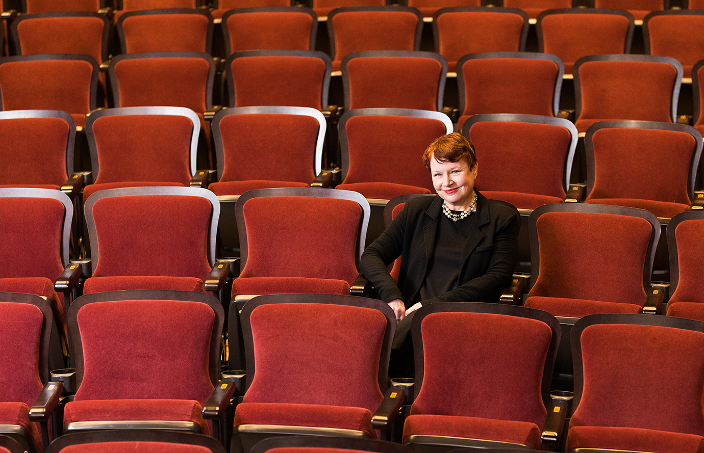 A woman sitting in a theatre, surrounded by red seats