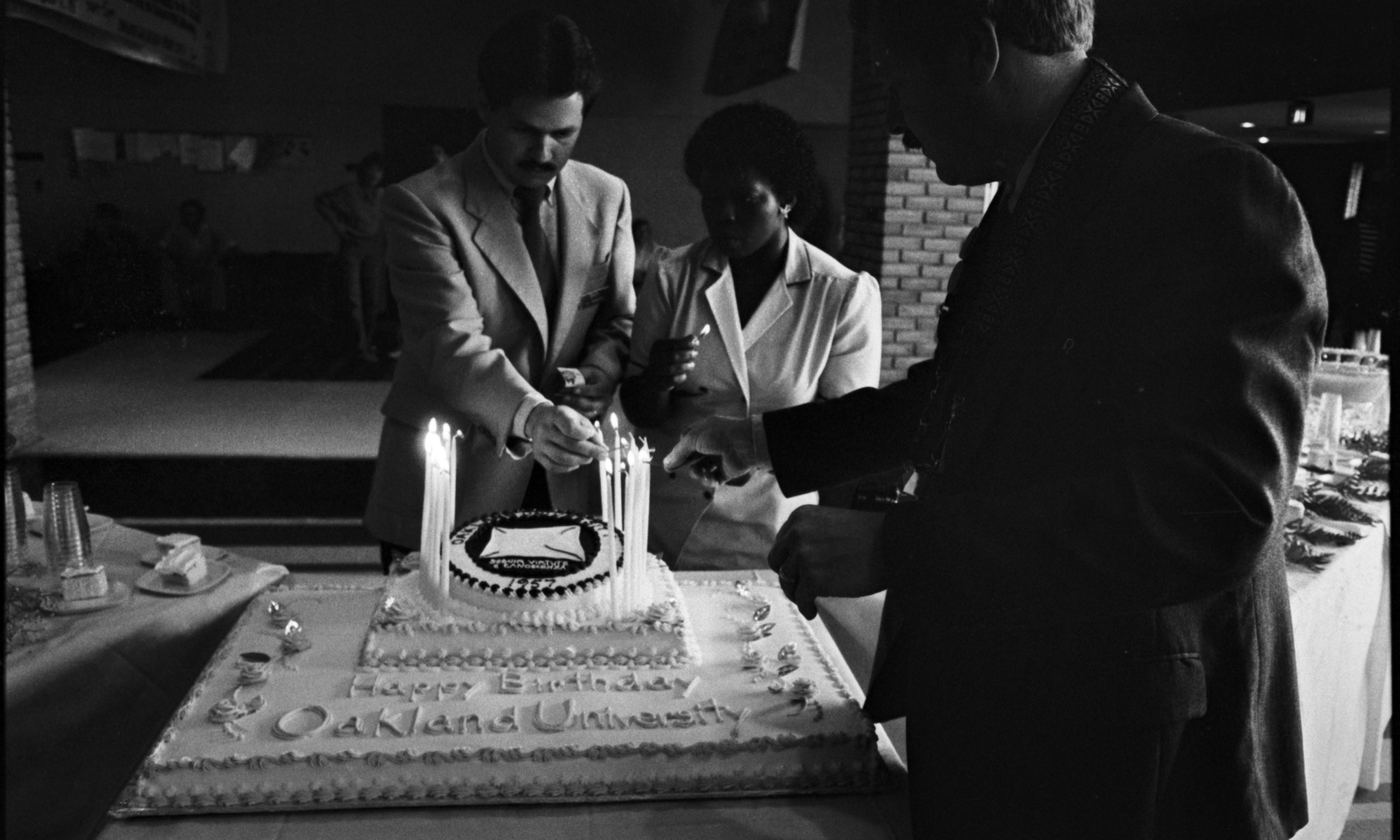 Three people lighting cake with text "Happy Birthday Oakland University"