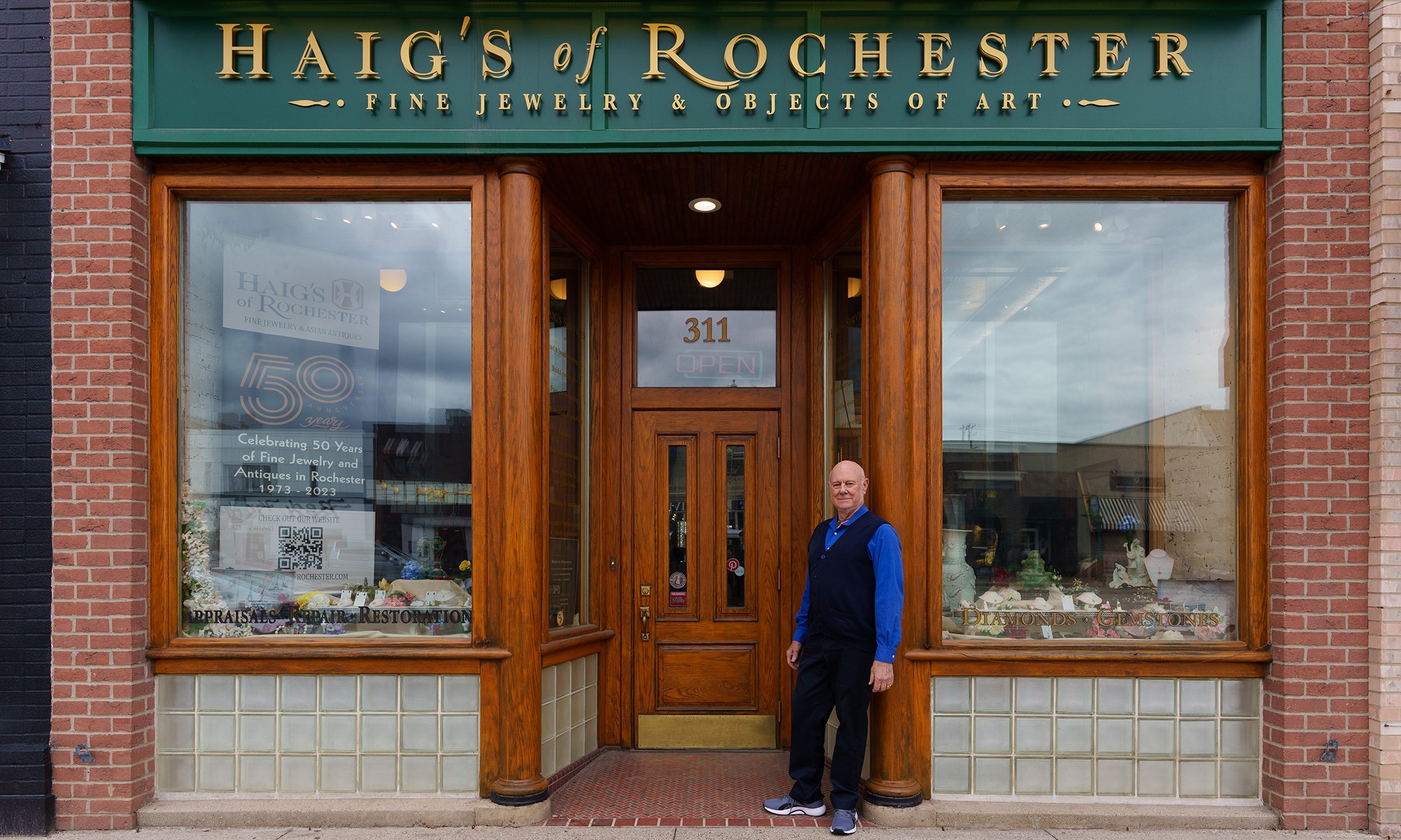 A man in front of his jewelry store with a sign that reads "Haig's of Rochester Fine Jewelry & Objects of Art"