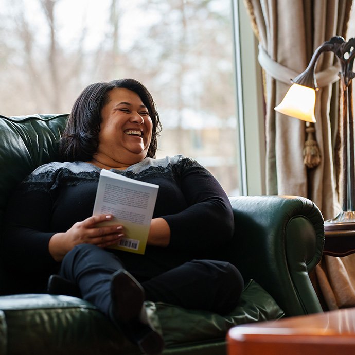 A woman sitting in a chair, holding a book and laughing