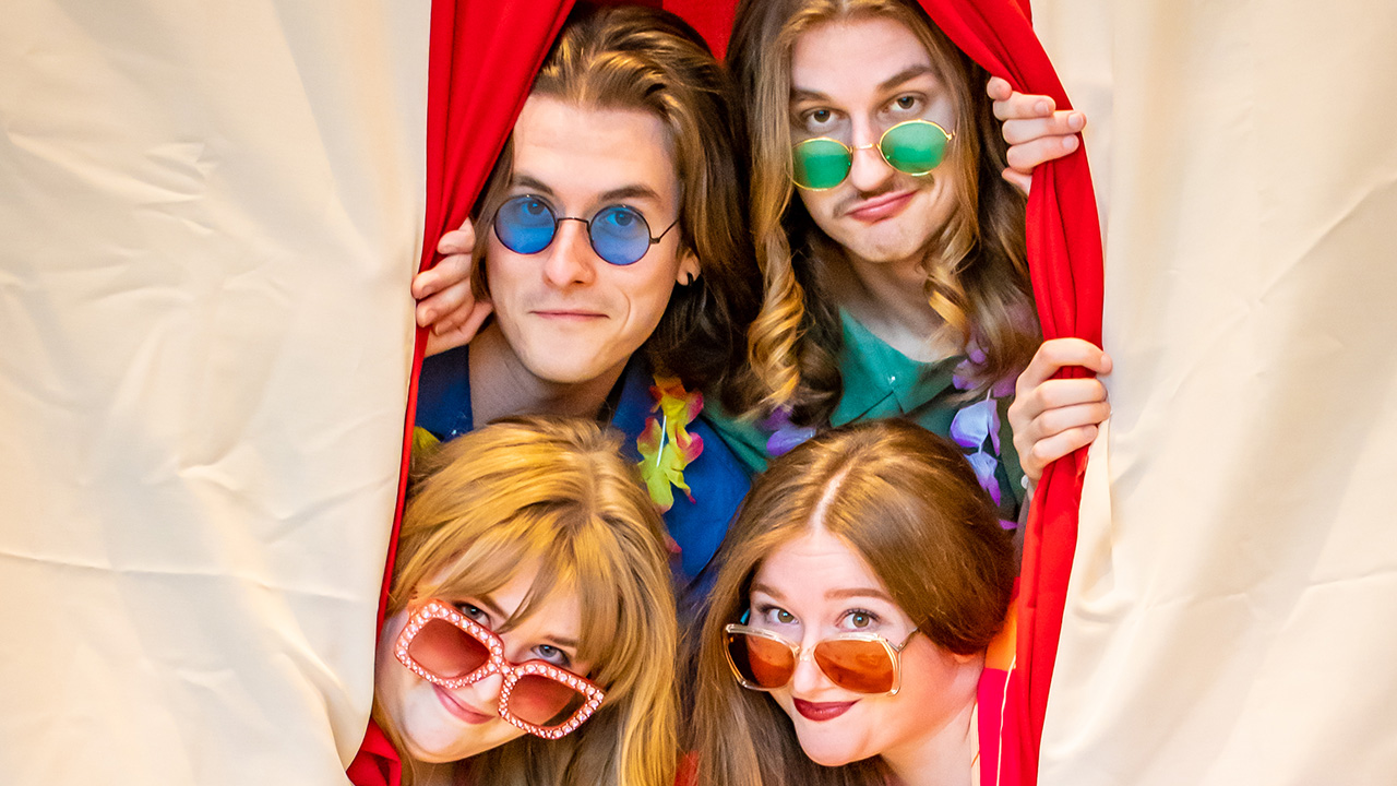 Four people, wearing sunglasses, poking their head out of a tent opening.
