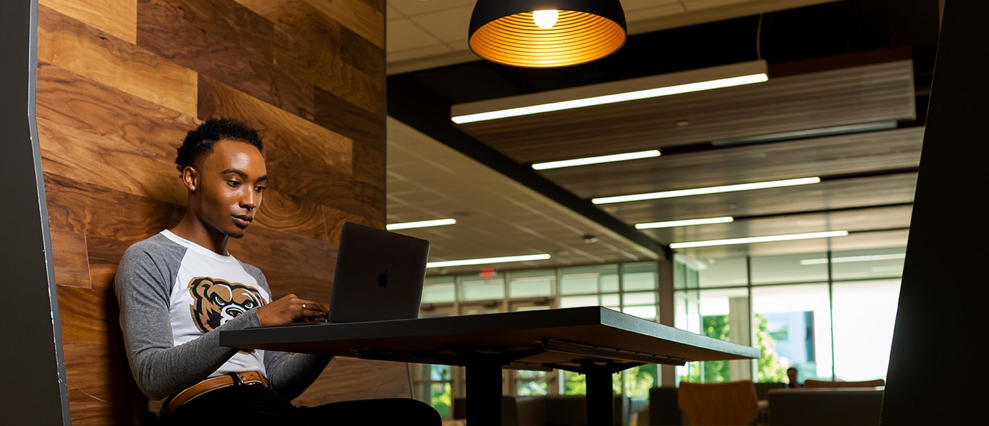 A student seated at a table with an open laptop in the Oakland Center.