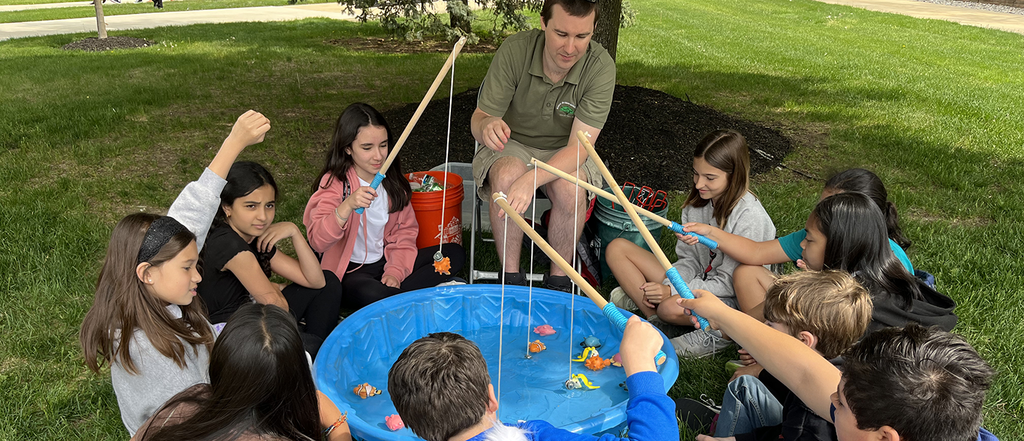 An instructor and kids play fishing in a kiddie pool.