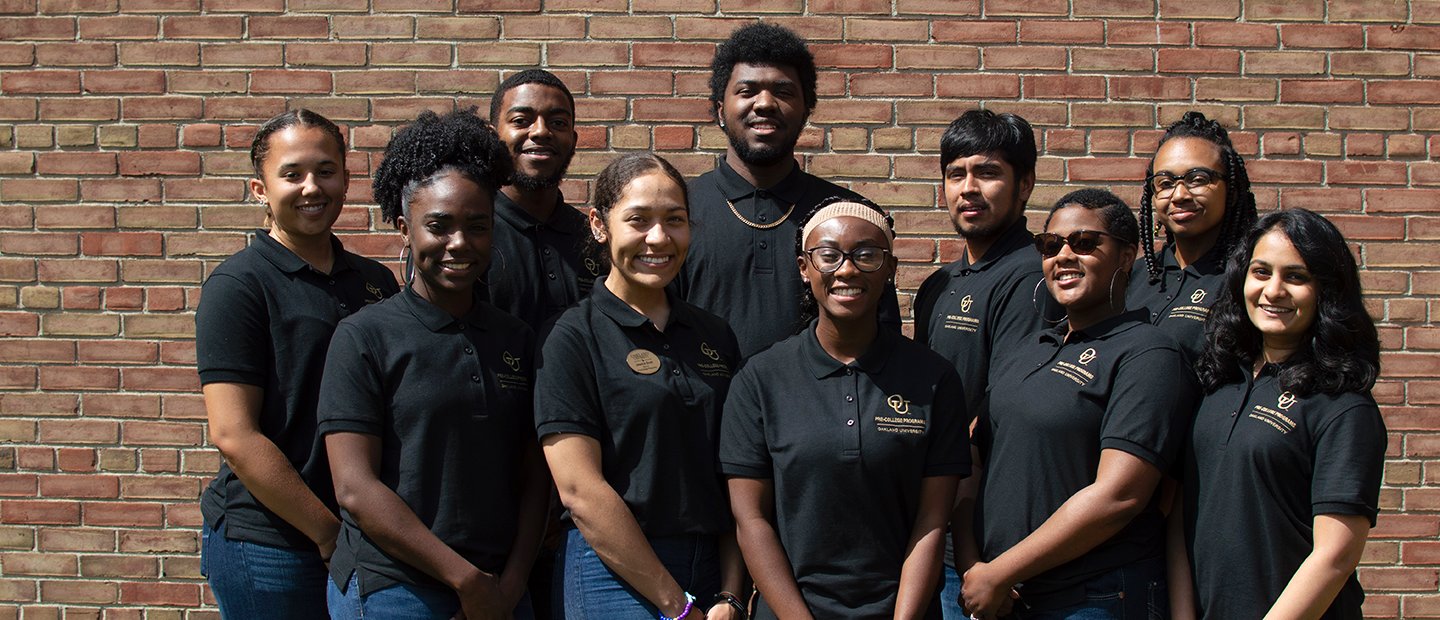 A group of Oakland University student employees wearing black shirts, posing in front of a brick wall.