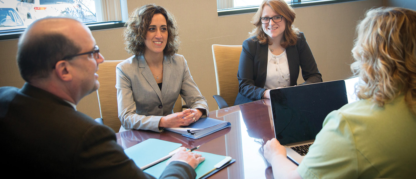 four adults with laptops and notepads seated around a table