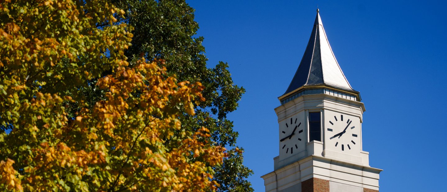 The top of Elliott clock tower next to a tree with green and orange leaves.