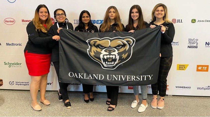 Women posing for a photo, holding an Oakland University banner.