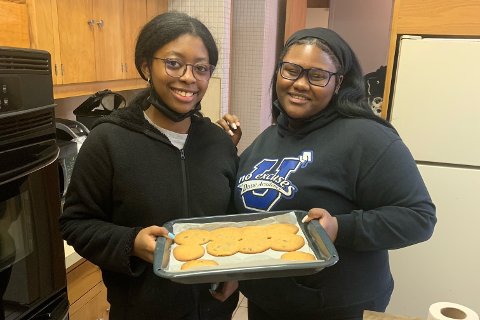 Two girls holding a baking tray with cookies on it.